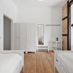 Zwei Betten, weiße Kleidung, Holzboden, Spiegel, Schrank und Lampe.