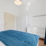 Bedroom with bed, crib, wardrobe, and window with curtain.