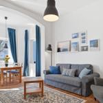 Living and dining area with sofa, chair, and table. Blue curtains and wall pictures.