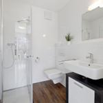 Badezimmer mit Dusche, Waschbecken und Toilette. Fliesenwand und Holzboden.