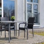 Terrasse mit Tisch und Stühlen vor einem Haus mit Fenstern und Balkon.