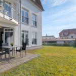 Haus mit Balkon, Terrasse und Garten. Im Hintergrund sind weitere Gebäude zu sehen.