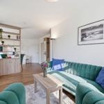 Ein Wohnzimmer mit grünem Sofa, Holztisch und Blick in die Küche.