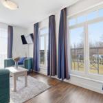Wohnzimmer mit Sofa, Couchtisch und TV. Große Fenster mit Blick auf Balkon.