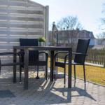 Außenbereich mit Tisch und drei Stühlen auf gepflastertem Boden.