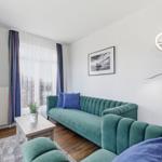 Ein Wohnzimmer mit grünem Sofa, blauen Kissen und einem Fernseher an der Wand.