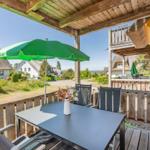 Terrasse mit Tisch, Stühlen und grünem Sonnenschirm. Blick auf Dächer und Grünflächen.