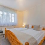 Schlafzimmer mit Holzbett, Nachttisch, Stuhl und Fenster mit Vorhängen.
