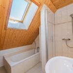 Badezimmer mit Dusche, Badewanne und Dachfenster. Holzdecke und Fliesenwand.