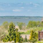 Haus mit Strohdach blickt auf einen See mit Wald im Hintergrund.