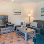 Wohnzimmer mit Sofa, Fernseher und Holztisch. Wandbilder zeigen Segelboote.
