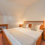 Schlafzimmer mit Holzbett, Nachttischen und Schreibtisch unter schrägem Dach.