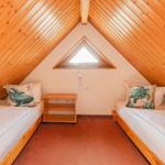 Zwei Betten unter Dachschrägen mit Holzdecke und Dreiecksfenster.