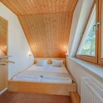 Schlafzimmer mit Holzdecke, Bett und Fenster mit Blick auf Bäume.