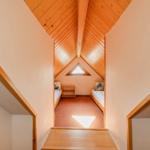 Zimmer mit Dachschrägen, zwei Betten und Dreiecksfenster. Holzdecke und Boden.