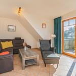 Wohnzimmer mit Sofa, Sessel und Terrasse. Durchgang zur Terrasse mit Tisch und Stühlen.