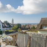 Terrasse mit Blick auf Dächer und Meer unter blauem Himmel mit weißen Wolken.