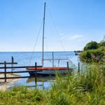 Segelboot liegt am Wasser, umgeben von Gras und einem Holzzaun.