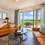Wohnzimmer mit Ledersofa, Glas-Tisch und Blick auf den See.