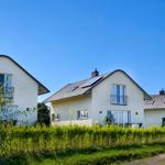 Drei moderne Häuser mit Balkonen und Solaranlagen unter blauem Himmel.
