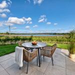 Terrasse mit Rattanmöbeln und Blick auf einen See.