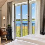 Schlafzimmer mit Blick auf See und Grünflächen durch geöffnete Balkontüren.