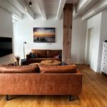 Wohnzimmer mit braunen Sofas, Holzboden und Wandbild. TV an der Wand.