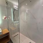 Shower with glass enclosure, marble wall, and wooden washbasin