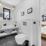 Badezimmer mit Waschbecken, Toilette und Fenster. Nebenraum mit Bett und Wandbild.