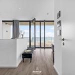 Moderne Wohnung mit Meerblick und Terrasse. Weiße Wände, Holzboden und Glasfront.