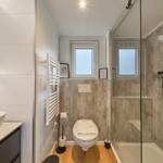 Badezimmer mit Dusche, Toilette und Waschbecken. Holzboden und Betonwand.