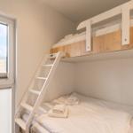 Zimmer mit Hochbett und Treppe, Fenster mit Jalousie, Bett mit weißen Laken und Handtüchern.