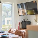Esszimmer mit Tisch, Stühlen und TV an der Wand. Fenster zeigt Außenbereich.
