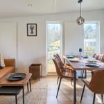 Wohn- und Essbereich mit braunem Sofa, Esstisch und Stühlen. Große Fenster und Wandbild.