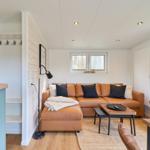 Wohnzimmer mit braunem Sofa, Holztisch und Fenster. Küchenbereich mit blauer Arbeitsplatte.