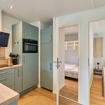 Küche mit hellen Schränken und Blick in zwei Schlafzimmer mit Betten.