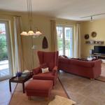 Living room with red armchair, sofa, and TV. Doorways to terrace and garden.