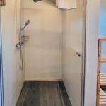 Shower cabin with overhead and handheld shower, dark floor, and white wall tiles.