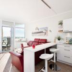 Living area with red sofa, white kitchen units, and view of balcony.