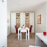 Dining room with white table, red chairs, and glass cabinets. Wooden floor and pendant lamp.