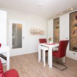 Living-dining area with white table, red chairs, and glass cabinets. Wooden floor and white walls.
