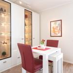 Dining room with white table, red chairs, and glass-front cabinets. Wall art and wooden floor.