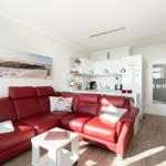 Red leather sofa in living area with kitchenette and wooden floor.