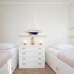 Two single beds flank a white dresser with sailboat model and lantern.