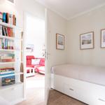 Bedroom with bed and bookcase. Passage to living room with red sofa.
