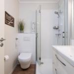 Bathroom with shower, sink, and toilet. White tiles and wooden floor.