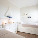 Room with two beds, dresser, and bookshelf with books and sailboat decoration.