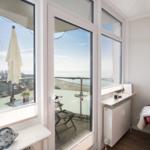 Room with view of balcony and sea, red armchair and windows with net.