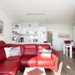 Living and dining area with red sofa, white kitchen, and dining set.