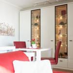 Dining area with white table, red chairs, and glass cabinets on the wall.